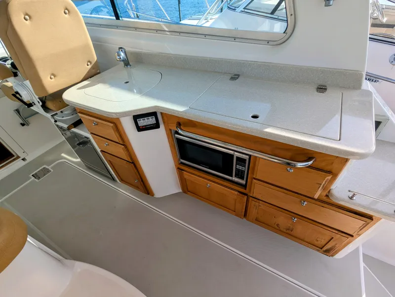 Slide: The Image of 2014 Back Cove 34 yacht interior with kitchenette, featuring sink, microwave, and wooden cabinetry. - 11