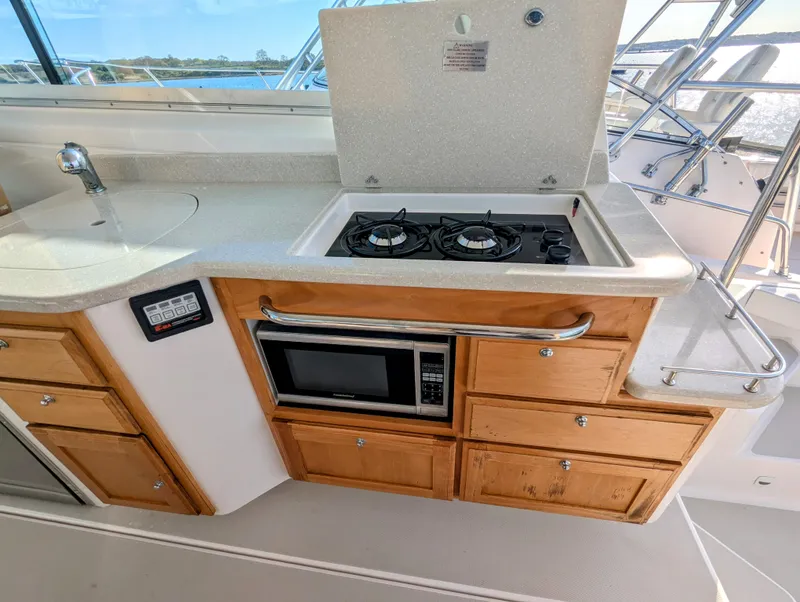 Slide: The Image of 2014 Back Cove 34 yacht kitchen with stove, microwave, and wooden cabinets. - 9