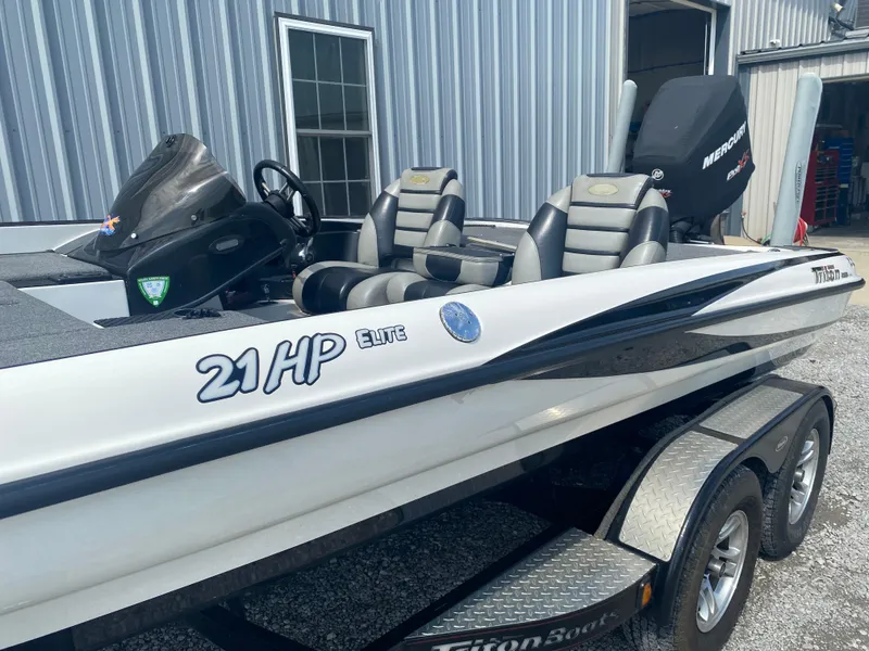 Slide: The Image of 2011 Triton 21 HP SC boat with dual seats and trailer, parked outside a metal building. - 7