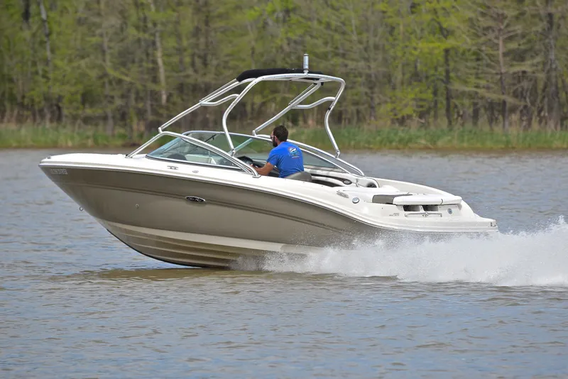 Slide: The Image of 2005 Sea Ray 220 Select boat cruising on a lake with a driver, surrounded by trees. - 4