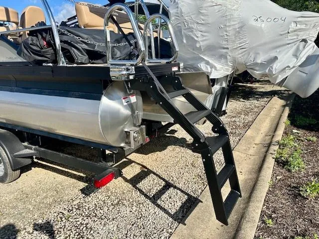 Slide: The Image of 2025 Barletta C24UE pontoon boat with rear ladder and cover, parked on gravel. - 22