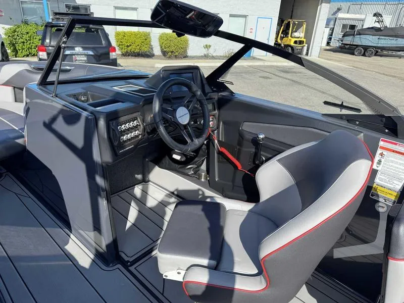 Slide: The Image of 2021 Moomba Craz boat interior with steering wheel and seating, parked outdoors. - 10