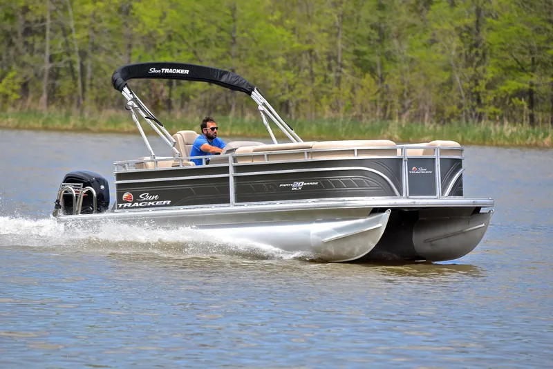 The Image of 2024 Sun Tracker Party Barge 20 DLX pontoon boat cruising on a lake. - 1