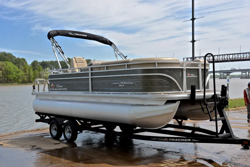 Slide: The Image of 2024 Sun Tracker Party Barge 20 DLX pontoon boat on trailer by a river. - 16