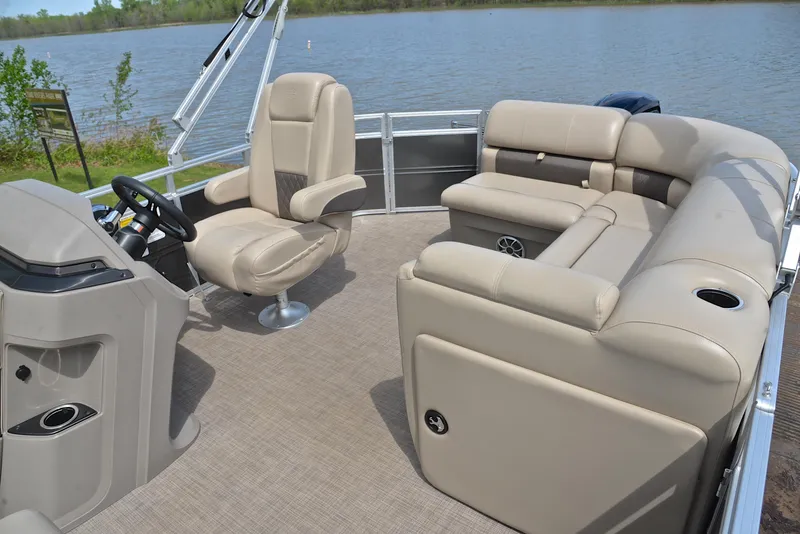 Slide: The Image of 2024 Sun Tracker Party Barge 20 DLX interior with beige seating and steering console by a lake. - 24