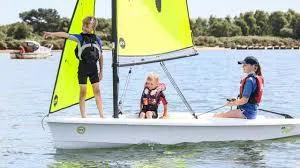 Slide: The Image of Three people sailing on a 2023 RS Zest boat with bright yellow sails. - 1