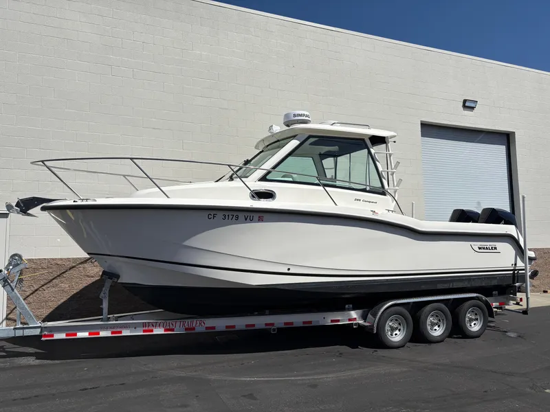 The Image of 2023 Boston Whaler 285 Conquest boat on a trailer, parked outside a building. - 0