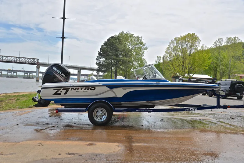 Slide: The Image of 2016 Nitro Z-7 Sport boat on trailer by riverside, with trees and bridge in background. - 15