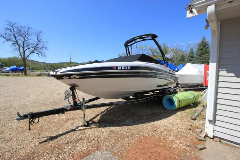 Slide: The Image of 2011 Glastron GLS 215 boat on trailer, parked outdoors under clear blue sky. - 2