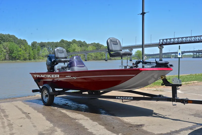 Slide: The Image of 2019 Bass Tracker Pro 170 boat on trailer by a river, under clear blue sky. - 16