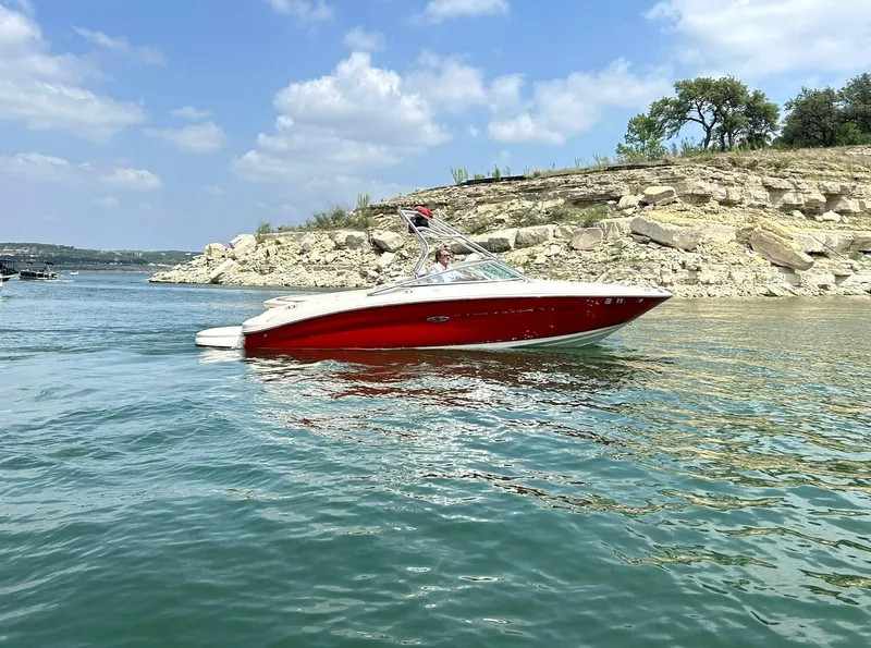 Slide: The Image of 2004 Sea Ray 240 Select boat cruising on a lake with rocky shoreline and blue sky. - 9