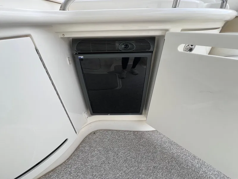 Slide: The Image of 2003 Sea Ray 290 Bowrider interior with open cabinet revealing a compact refrigerator. - 31