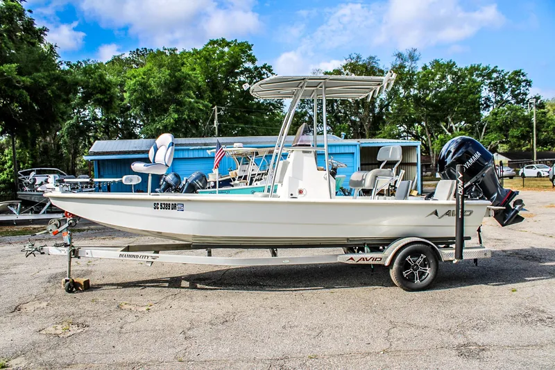 Slide: The Image of 2021 Avid 21 FS boat on trailer, parked outdoors with trees and blue sky background. - 0