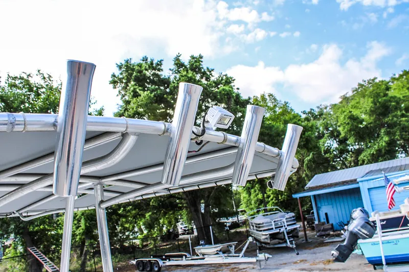 Slide: The Image of 2021 Avid 21 FS boat with rod holders, parked near trailers and trees. - 10