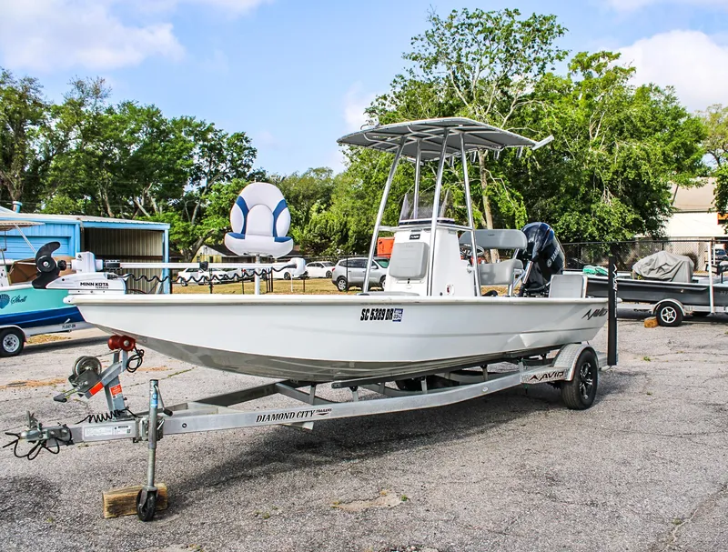 Slide: The Image of 2021 Avid 21 FS boat on trailer, parked outdoors with trees in background. - 2