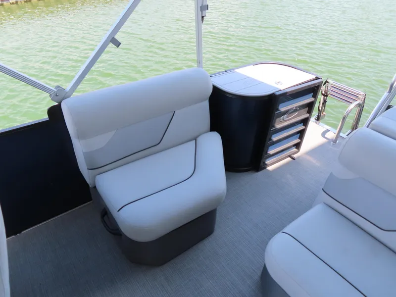 Slide: The Image of 2022 Crest Classic LX 220 boat interior with cushioned seating and storage, on calm water. - 12