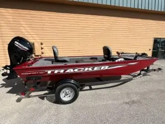 Slide: The Image of 2025 Tracker Panfish 17 boat, red exterior, parked outdoors, featuring a Mercury outboard motor. - 36