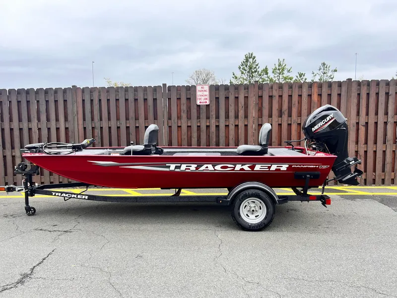 The Image of 2025 Tracker Panfish 17 boat on trailer, red color, parked by wooden fence. - 0