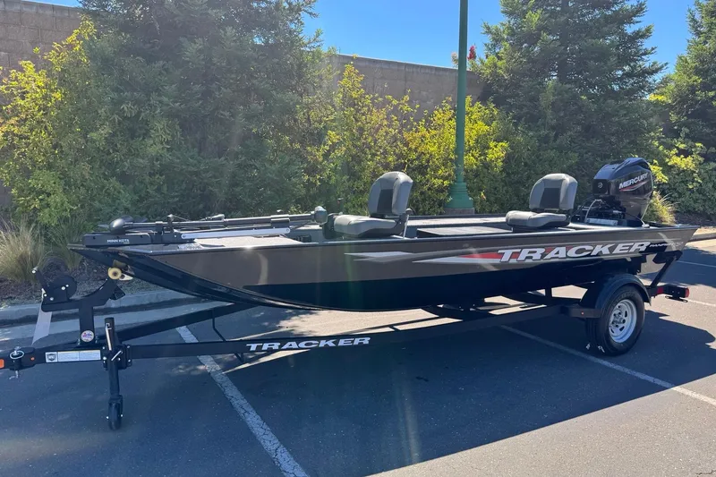 Slide: The Image of 2025 Tracker Panfish 17 boat on trailer in parking lot, surrounded by greenery. - 2