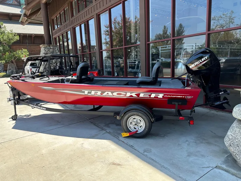 Slide: The Image of 2025 Tracker Panfish 17 boat with Mercury engine, parked outside a building. - 2
