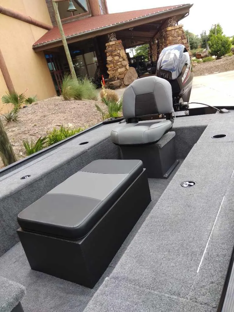 Slide: The Image of 2025 Tracker Panfish 17 boat interior with seating and motor, parked near a rustic building. - 3