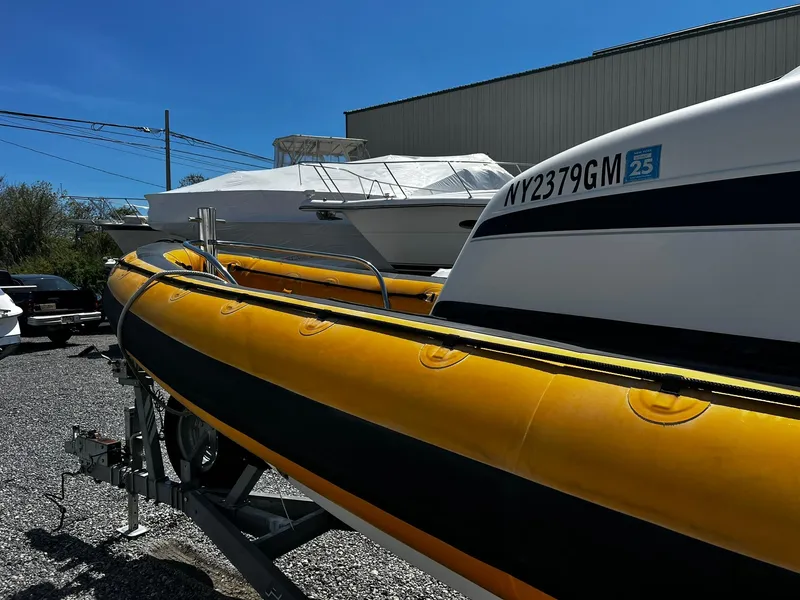 Slide: The Image of 2013 Protector Targa 30 boat with yellow inflatable sides on a trailer, parked outdoors. - 12