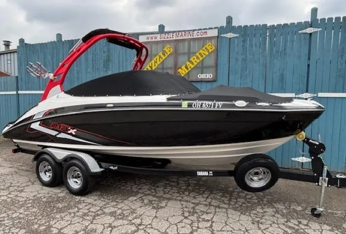 Slide: The Image of 2018 Yamaha Boats 212X on trailer, black and red design, parked by blue fence. - 41
