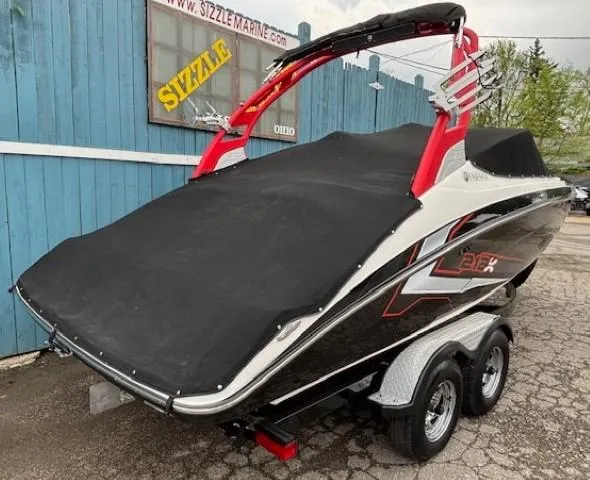 Slide: The Image of 2018 Yamaha Boats 212X covered, parked on a trailer near a blue building. - 42