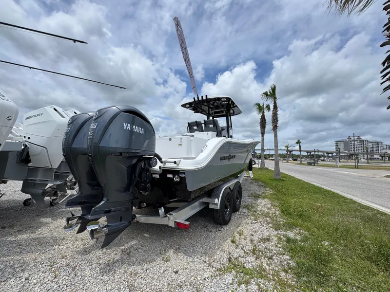 Slide: The Image of 2025 NauticStar 292 Legacy boat with dual outboard engines on a trailer, parked near palm trees. - 10
