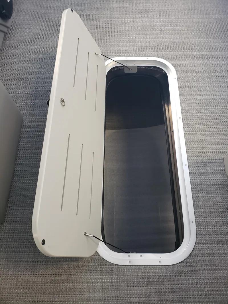 Slide: The Image of 2025 Bentley Pontoons Legacy Swingback storage compartment with open hatch on textured flooring. - 7