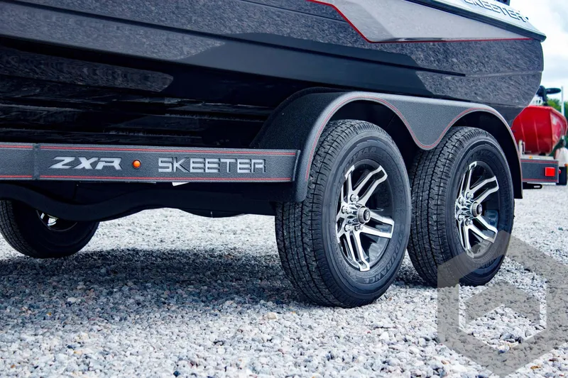 Slide: The Image of 2025 Skeeter ZXR 21 boat trailer with dual wheels on gravel surface. - 9