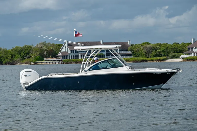 Slide: The Image of 2021 Pursuit DC 246 Dual Console boat on water, with American flag and scenic background. - 10