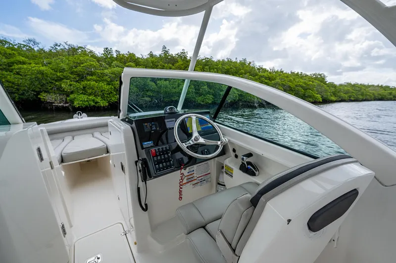 Slide: The Image of 2021 Pursuit DC 246 Dual Console boat interior with steering wheel, near lush greenery and water. - 36