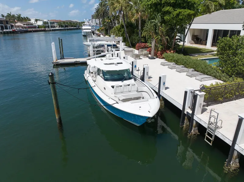 Slide: The Image of 2023 Tiara Yachts 48 LS docked by a waterfront home, surrounded by lush greenery. - 2