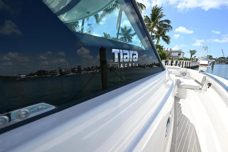 Slide: The Image of 2023 Tiara Yachts 48 LS reflecting water and palm trees, docked in a sunny marina. - 24
