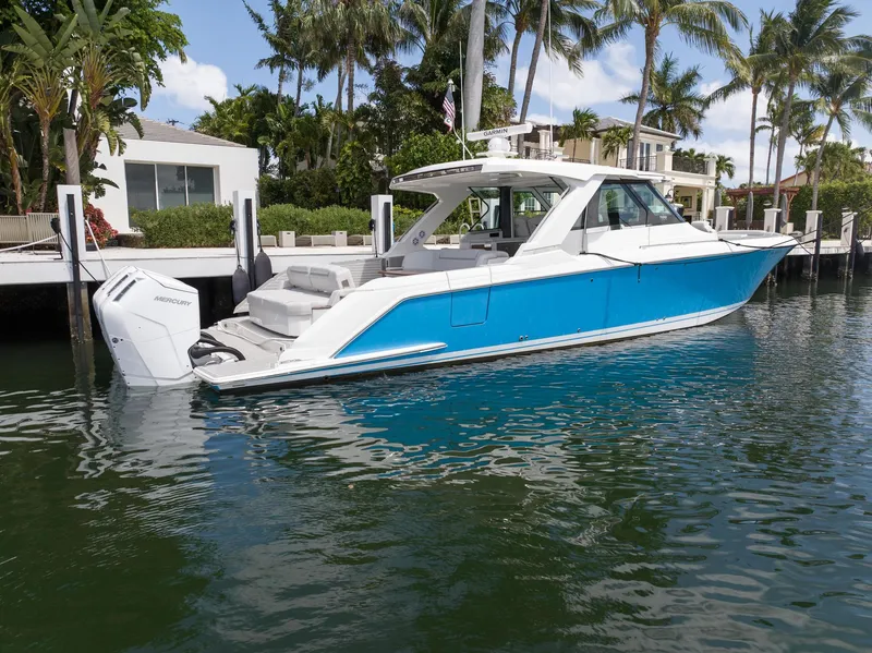 Slide: The Image of 2023 Tiara Yachts 48 LS in vibrant blue, docked by palm trees. - 7