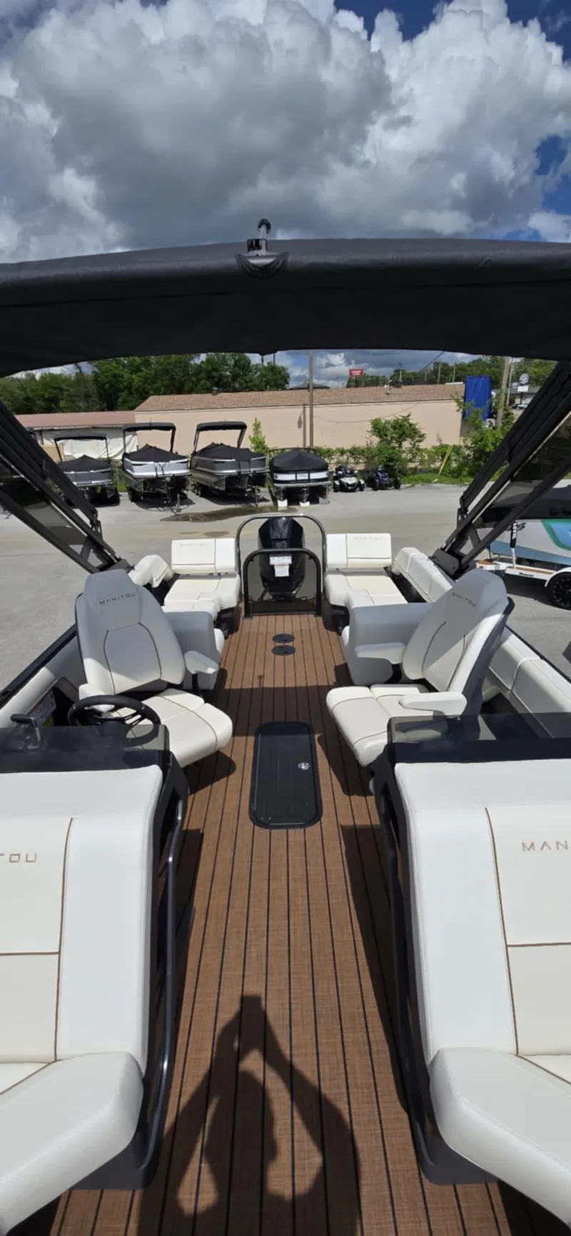 Slide: The Image of 2025 Manitou Explore boat interior with sleek seating and wooden deck under a cloudy sky. - 10