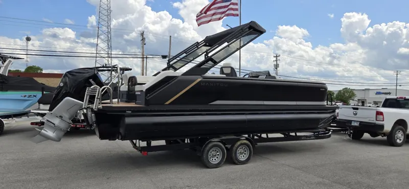 Slide: The Image of 2025 Manitou Explore pontoon boat on trailer, parked outdoors under cloudy sky. - 3
