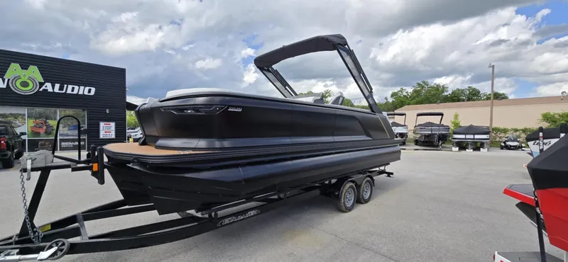 Slide: The Image of 2025 Manitou Explore boat on trailer, parked outdoors under cloudy sky. - 4