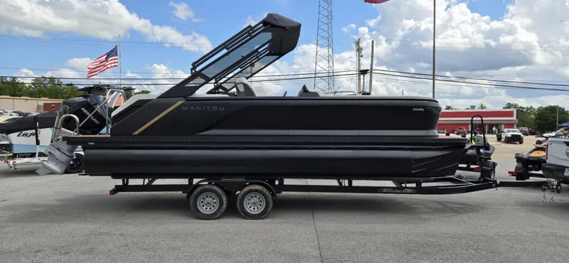 Slide: The Image of 2025 Manitou Explore pontoon boat on trailer, parked outdoors under cloudy sky. - 5
