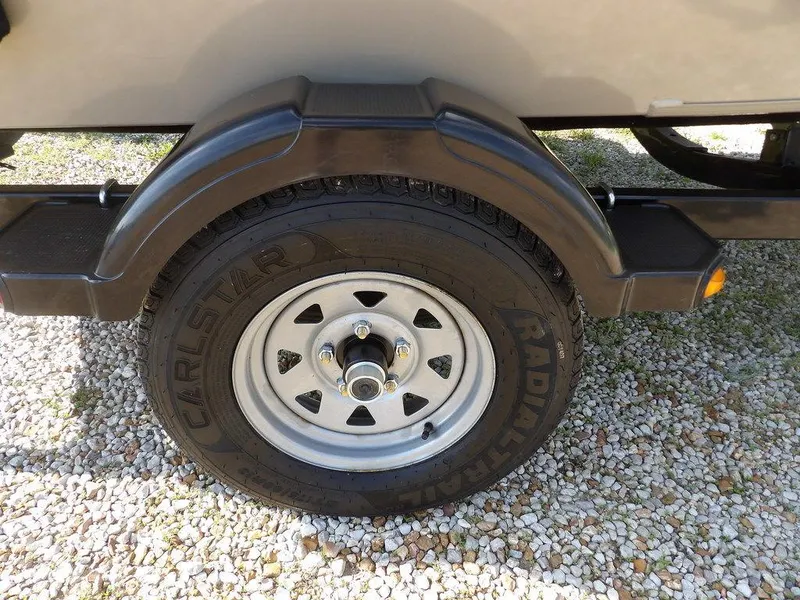 Slide: The Image of Trailer wheel with Carlstar tire on a 2006 Lowe FM165SC, parked on gravel. - 2