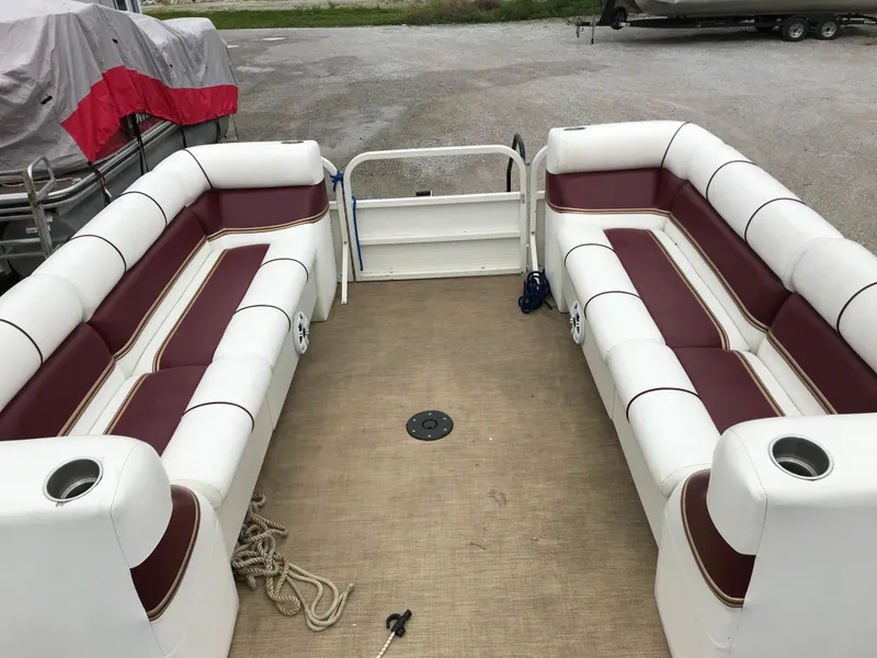 Slide: The Image of 2005 Bentley Pontoons 243 interior with white and maroon seating, docked on a gravel surface. - 25
