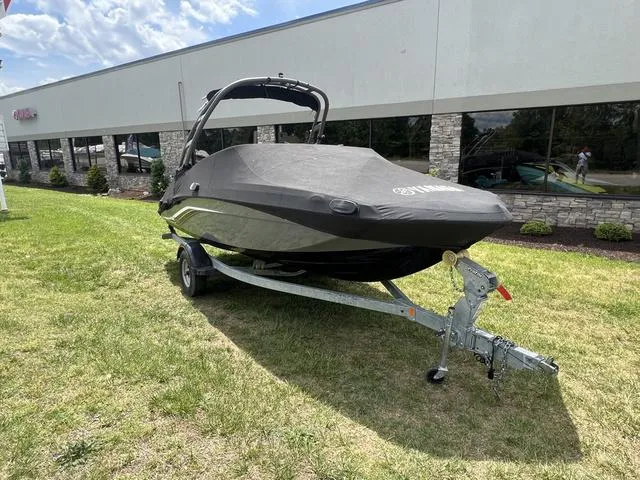 Slide: The Image of 2019 Yamaha Boats AR195 on trailer with cover, parked on grass near building. - 10
