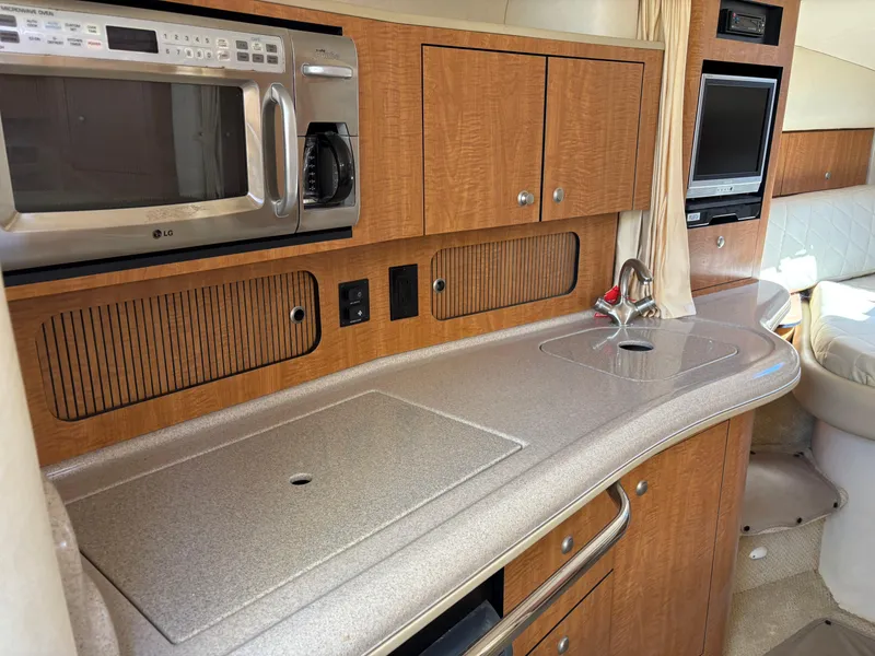 Slide: The Image of 2006 Sea Ray 320 Sundancer interior kitchen with microwave, sink, and TV. - 13
