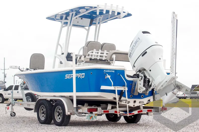 Slide: The Image of 2023 Sea Pro 208 Bay boat on trailer, blue hull, white motor, parked on gravel. - 13
