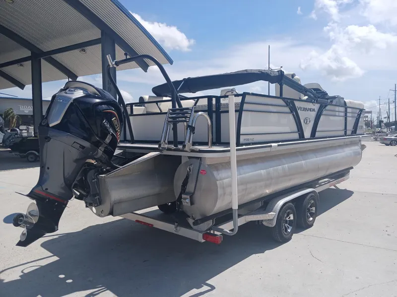 Slide: The Image of 2023 Veranda VP22VLC pontoon boat with outboard motor on trailer, parked outdoors. - 2