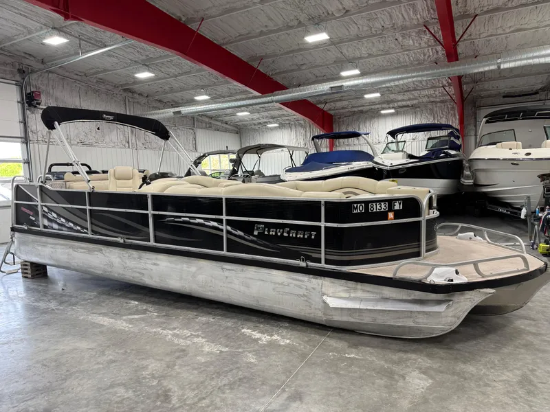 Slide: The Image of 2012 PlayCraft 2700 Extreme pontoon boat in indoor showroom, black exterior, beige seating. - 2