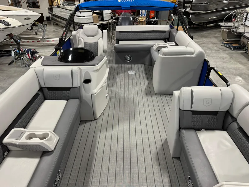 Slide: The Image of 2023 Sweetwater 2286 pontoon boat interior with gray seating and blue canopy in a showroom. - 11