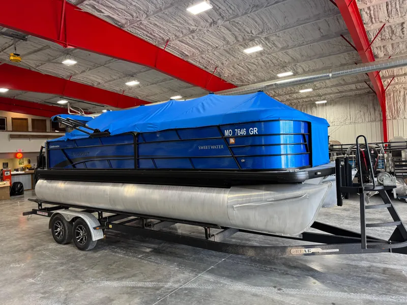 Slide: The Image of 2023 Sweetwater 2286 pontoon boat with blue cover on trailer in indoor storage. - 7