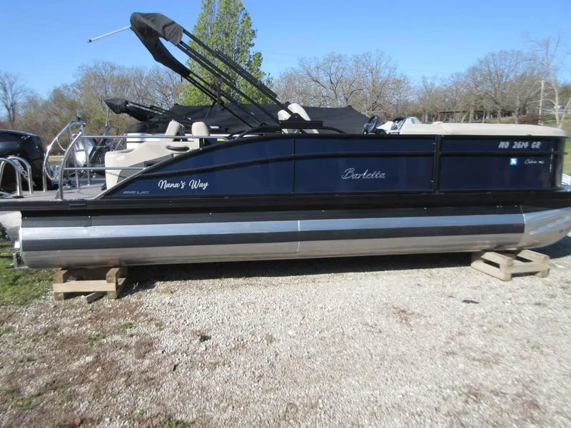 Slide: The Image of 2022 Barletta Cabrio 22UC pontoon boat on gravel, side view, with black canopy. - 21